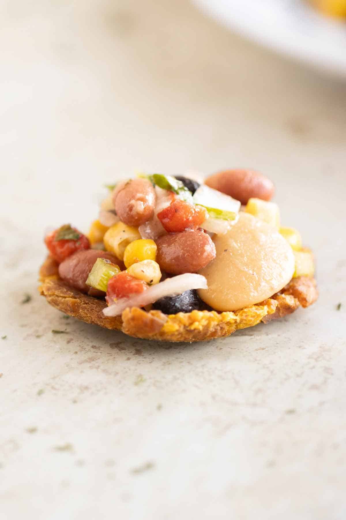 A fired plantains toston topped with a bean salad.