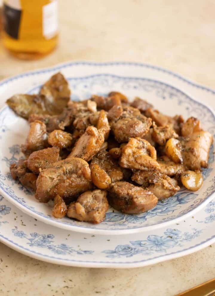 A plate with a Spanish Pollo al ajillo on a plate and a beer on the background.