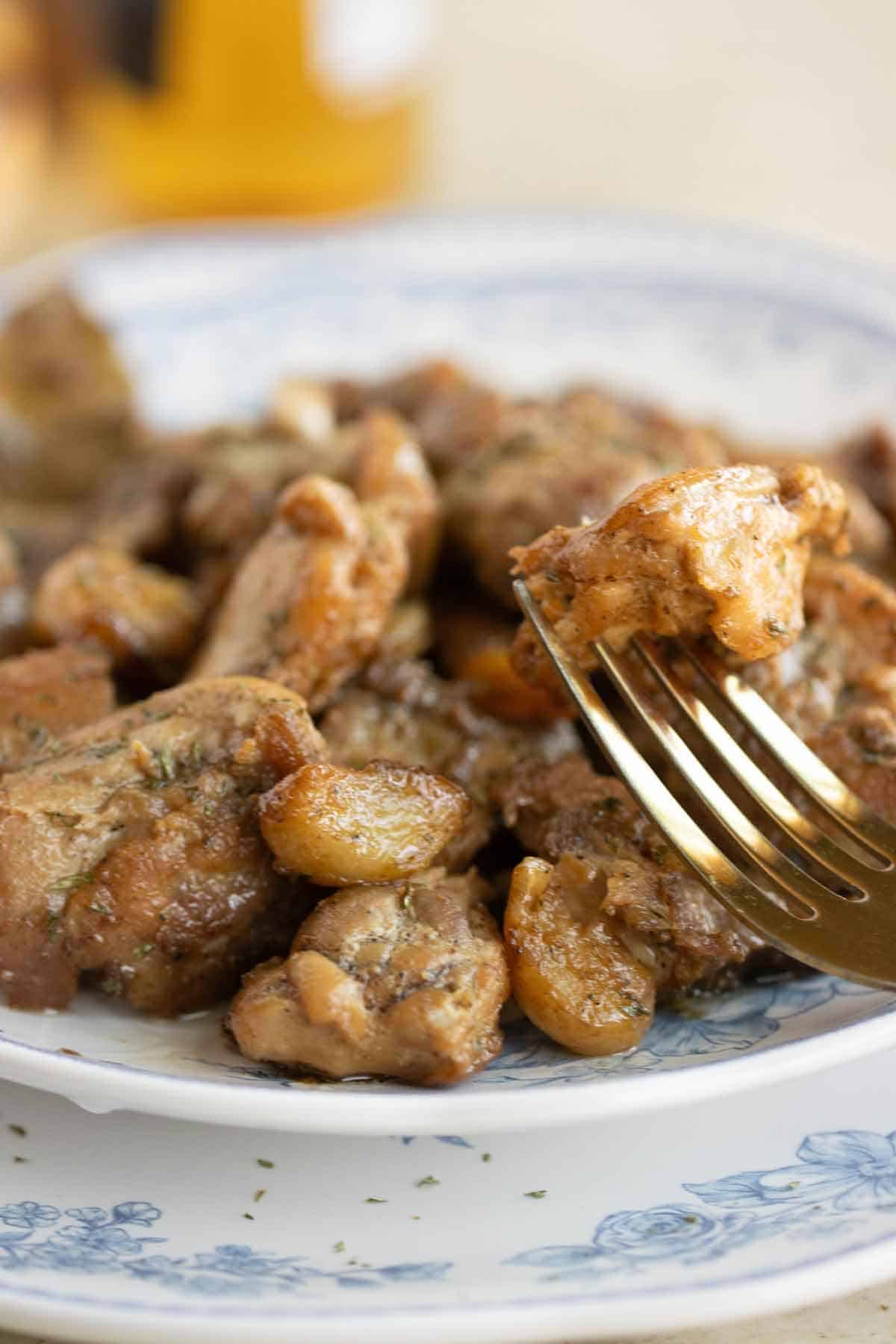 A plate of spanish pollo al ajillo and a fork with a piece of chicken.