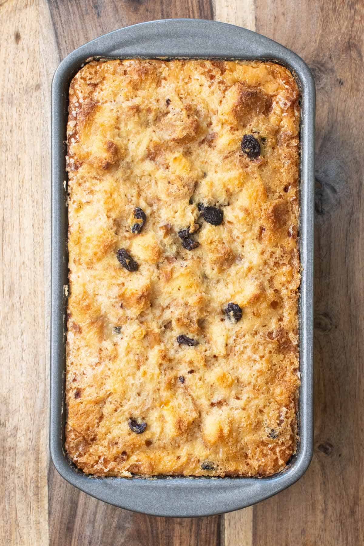 A loaf pan of a bread pudding on a loaf pan mold on top of a wodd cutting board.