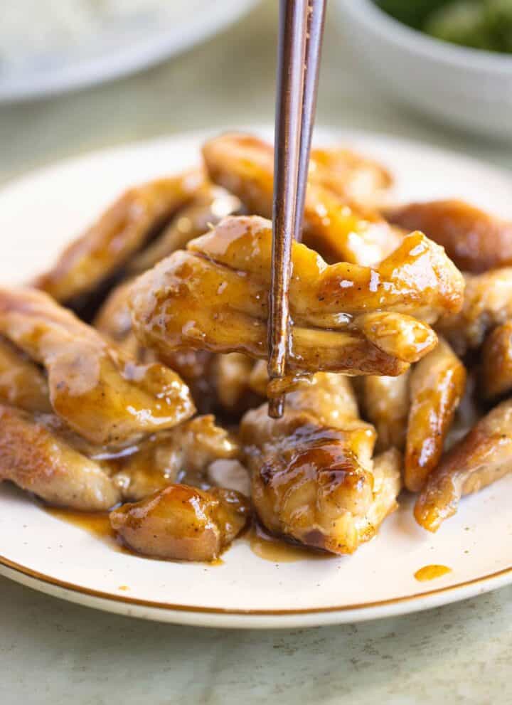 A late of chicken teriyaki and on the front a piece of chicken on chopsticks.