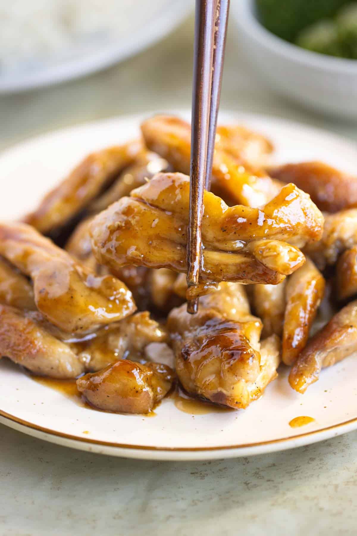 A late of chicken teriyaki and on the front a piece of chicken on chopsticks.