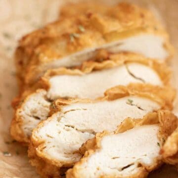 a crispy fried chicken breast cut into thick slices over a plate with parchment paper.