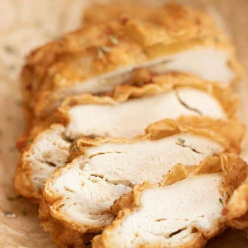 a crispy fried chicken breast cut into thick slices over a plate with parchment paper.