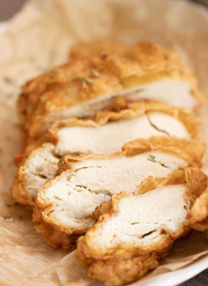 a crispy fried chicken breast cut into thick slices over a plate with parchment paper.