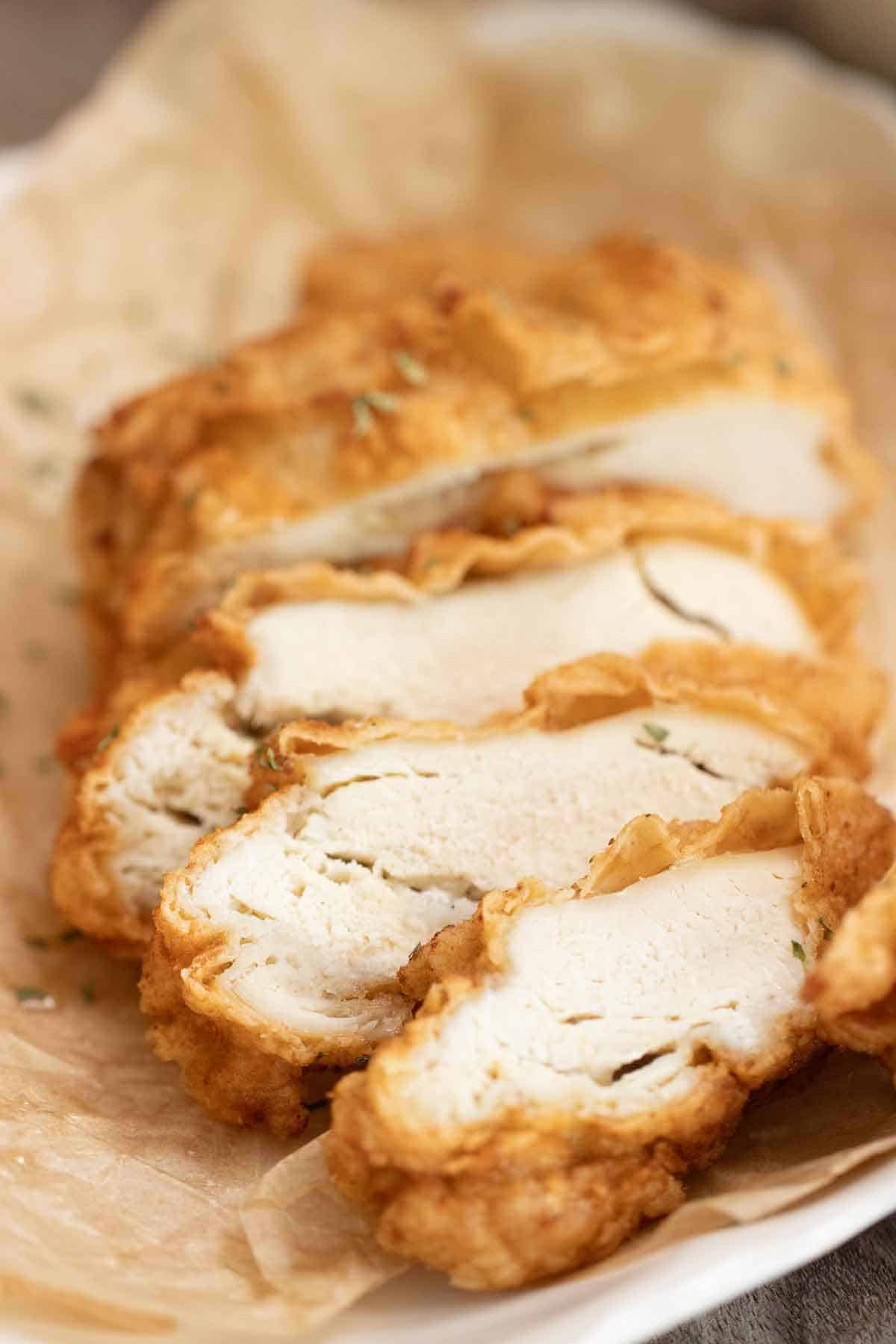 a crispy fried chicken breast cut into thick slices over a plate with parchment paper.
