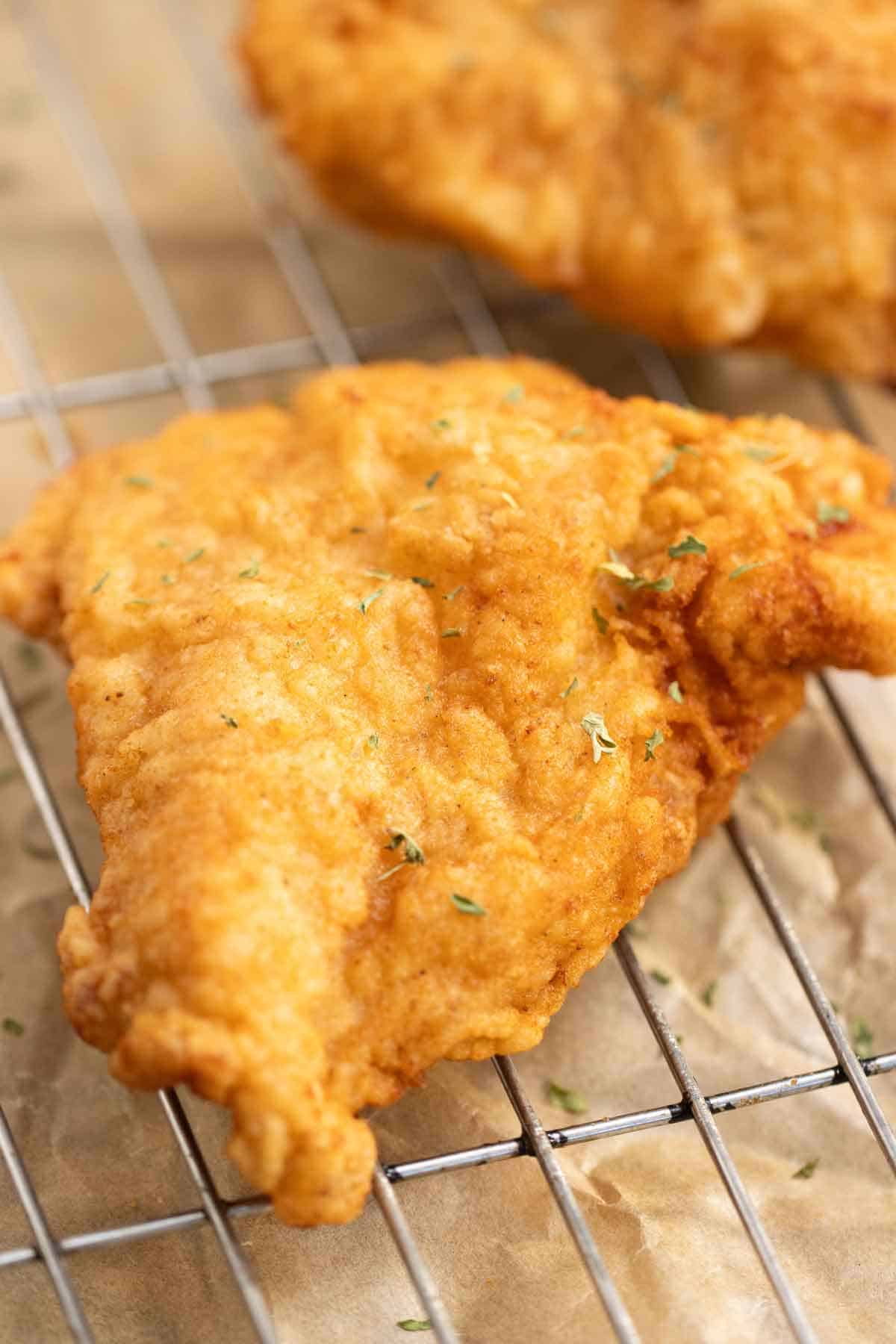 2 pieces of crispy fried chicken breast over a metal rack.