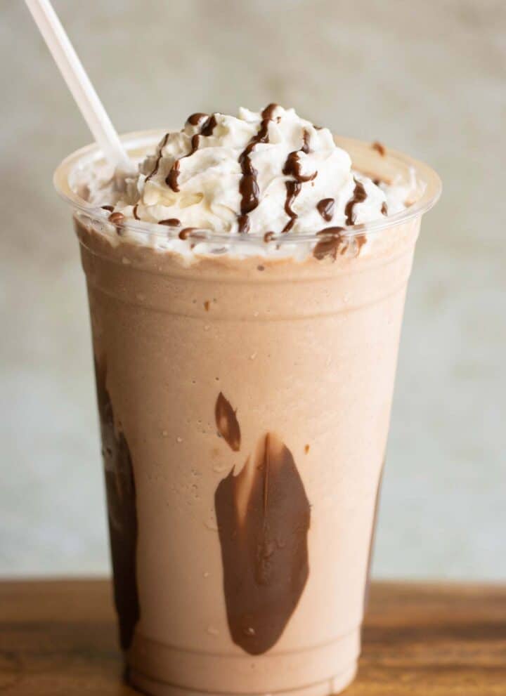 A large cup with a Nutella Frappe with whipped cream and chocolate drizzle with a straw.