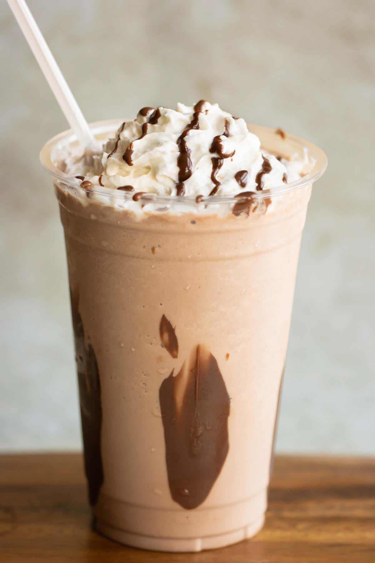 A large cup with a Nutella Frappe with whipped cream and chocolate drizzle with a straw.