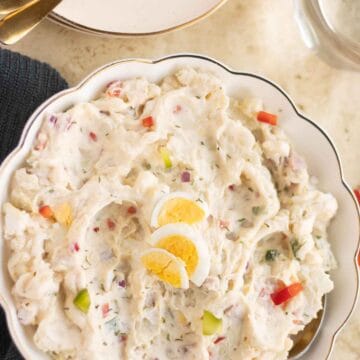 A plate with a puerto rican ensalada de papa with a couple of plates on the side with forks.