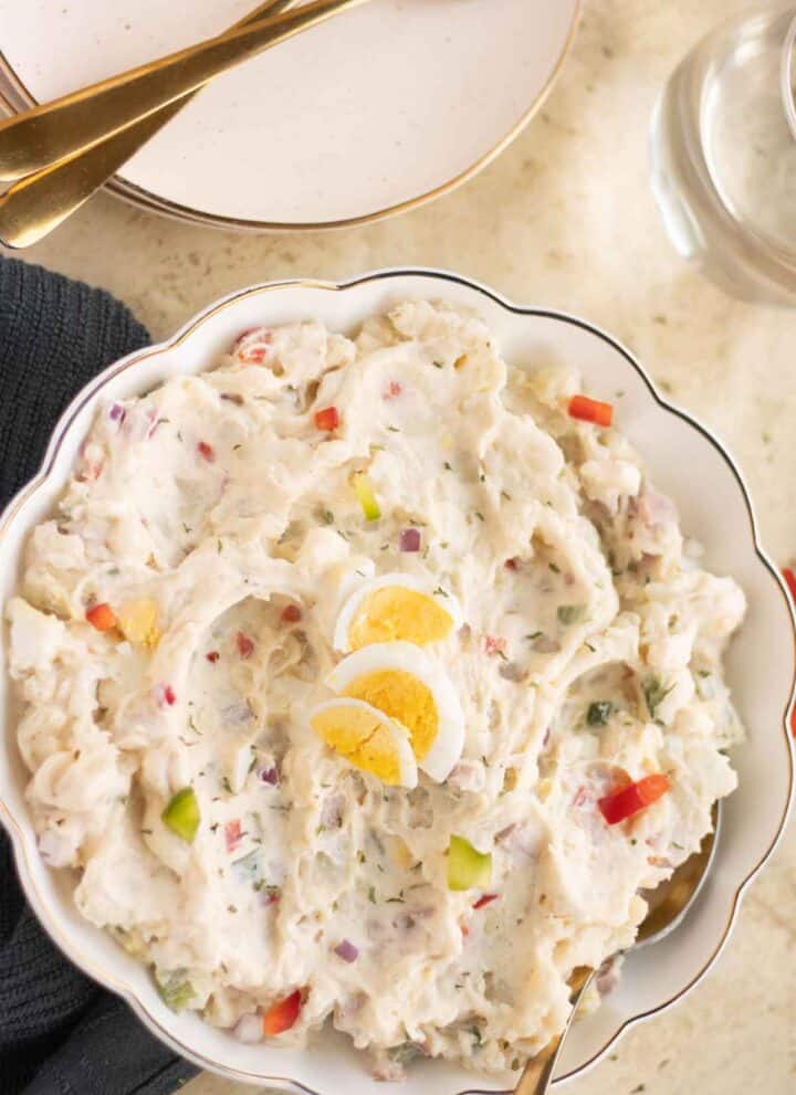 A plate with a puerto rican ensalada de papa with a couple of plates on the side with forks.