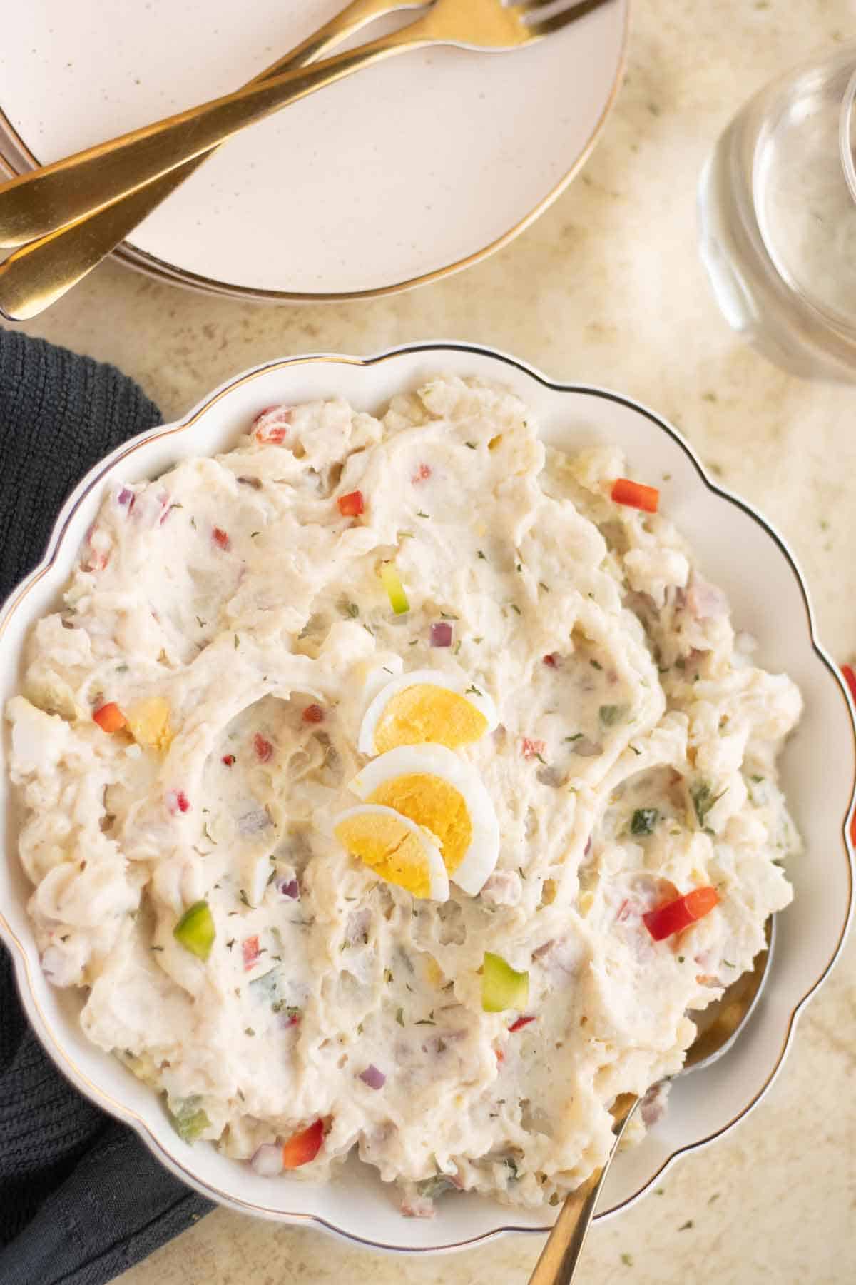 A plate with a puerto rican ensalada de papa with a couple of plates on the side with forks.