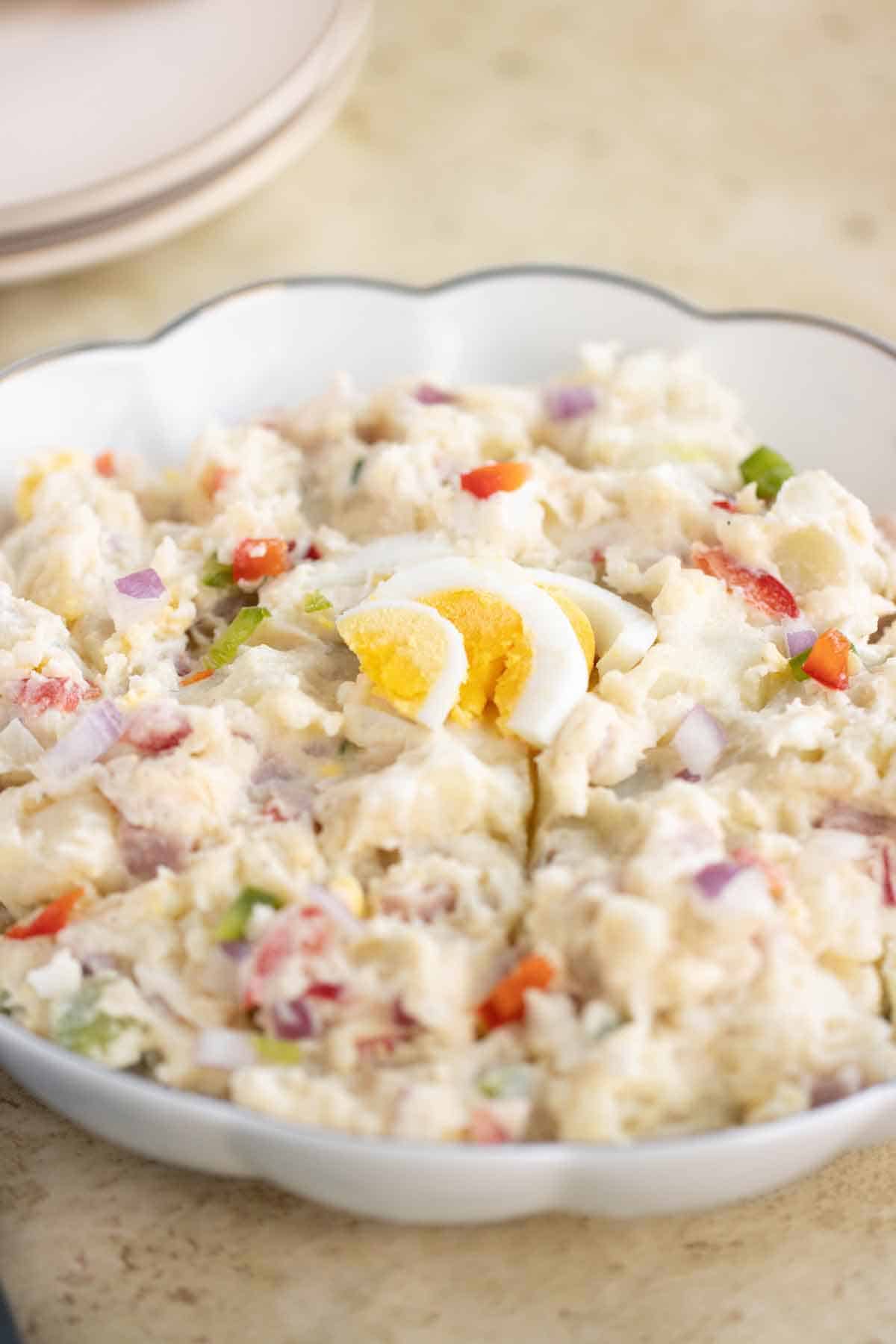 A big plate with a puerto rican potato salad and a couple of plates on the background.