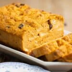A big loaf of a pumpkin bread pudding with a few cut slices and a slice on a plate on the front.