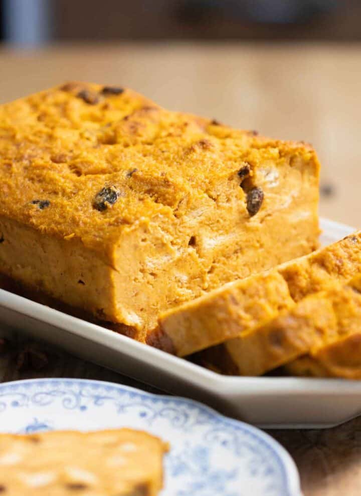 A big loaf of a pumpkin bread pudding with a few cut slices and a slice on a plate on the front.