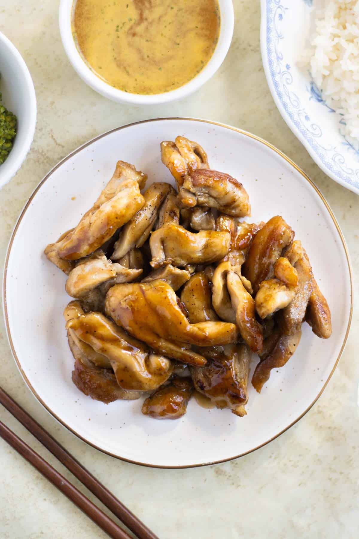 A plate of sweet chicken teriyaki with a dish of broccoli, white rice, and soup around.