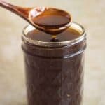 A jar full os sweet teriyaki sauce and a spoon dripping sauce.