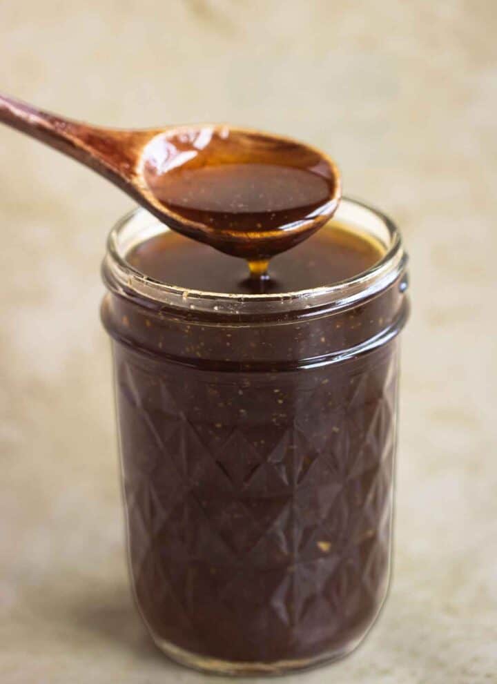 A jar full os sweet teriyaki sauce and a spoon dripping sauce.