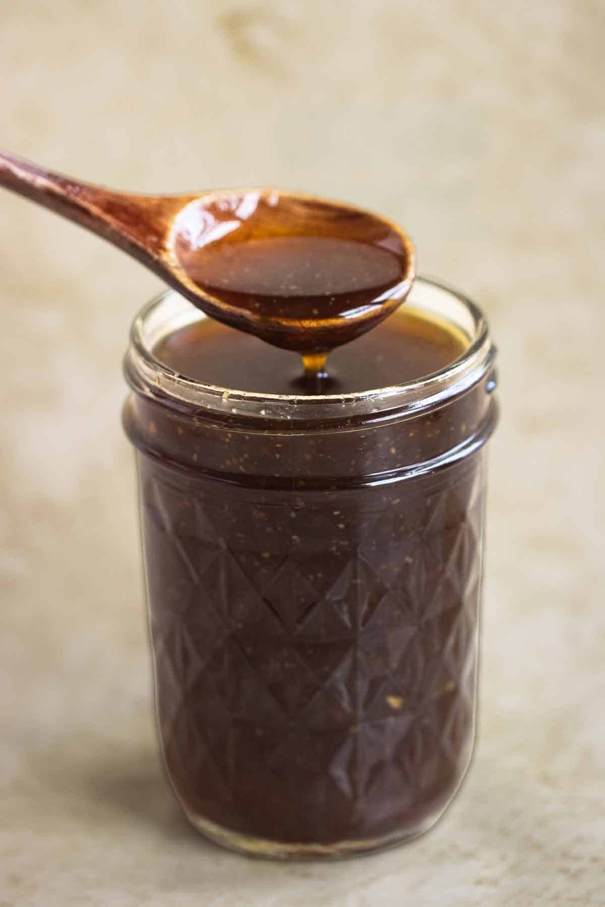A jar full os sweet teriyaki sauce and a spoon dripping sauce.
